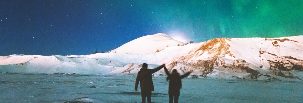 Couple Travelers Enjoying Northern Lights View Above Mountains Raised Hands Travel Lifestyle And Relationship Man And Woman Concept Vacations Into The Wild Night Scene