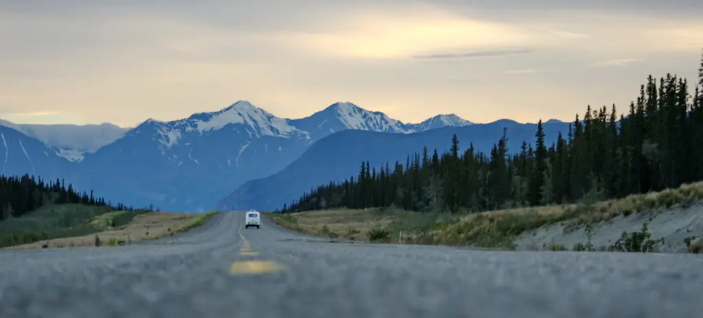 Car driving down a road toward a snowy mountain range