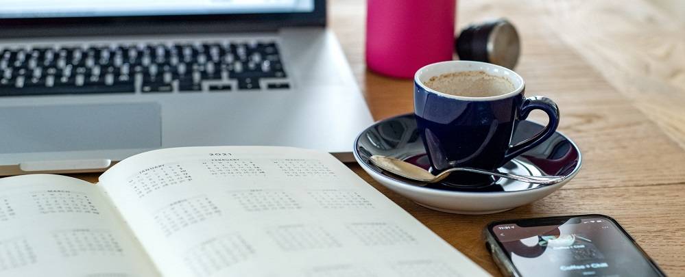 Cup of espresso and an open calendar in front of a laptop