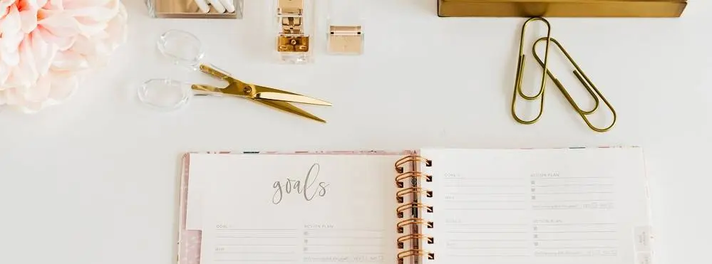 Desk surface with office suppliers and a planner that says goals