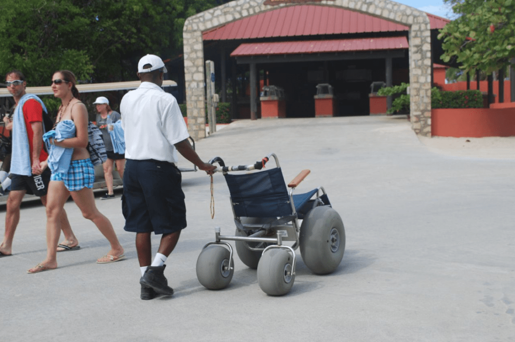 Man pushing beach wheelchair with large wheels along pathway