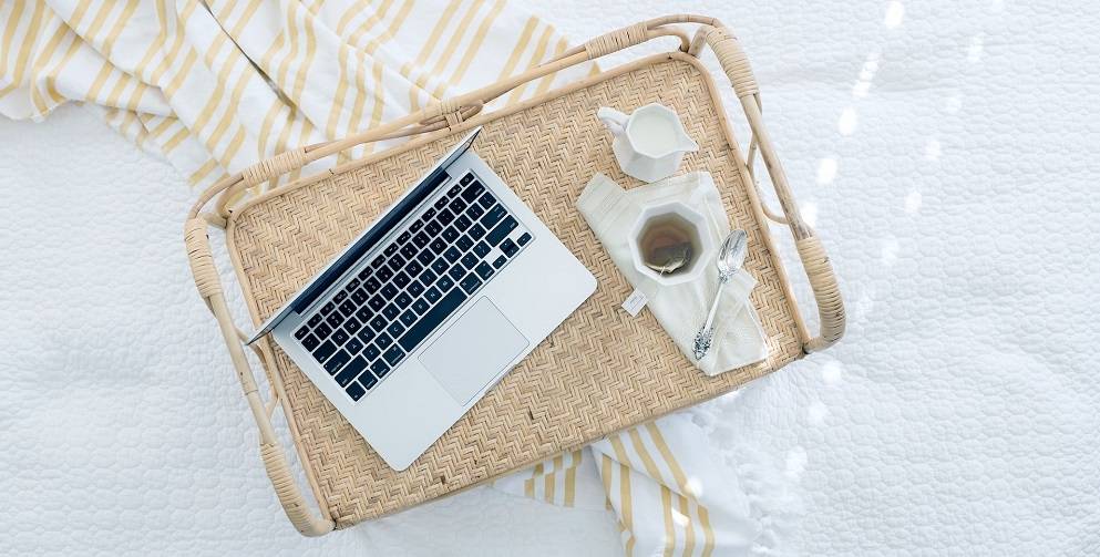 a tray containing a laptop and cup of coffee sits on top of a blanket