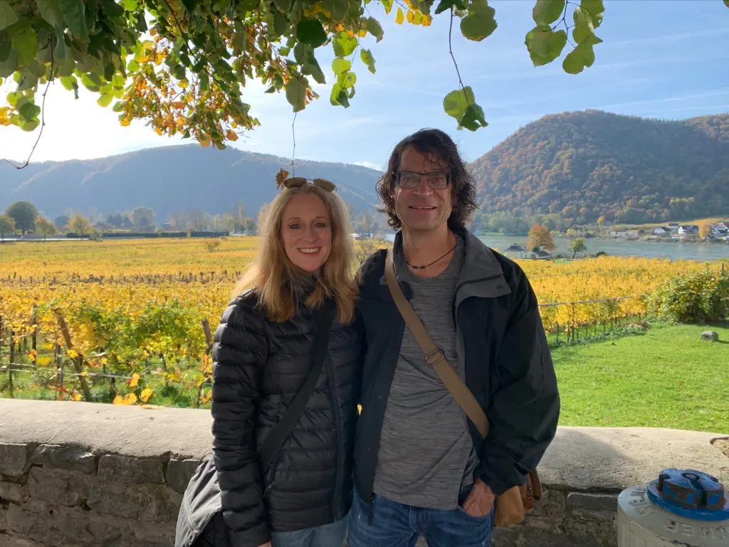 A couple stands overlooking a vineyard and river valley