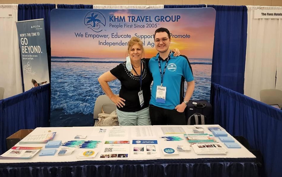 Joanne and Zach posing in front of KHM Travel Group booth at Travel Agent Forum at the trade show