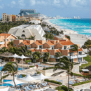 large resort property surrounding swimming pools and palm trees that stretch to a white sand beach and turquoise sea with resorts in the distance