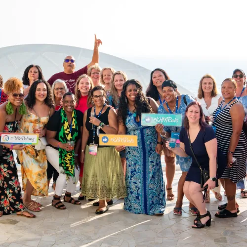 KHM Travel agents posing for a picture while holding signs that say, 'You Belong at KHM Travel Group'